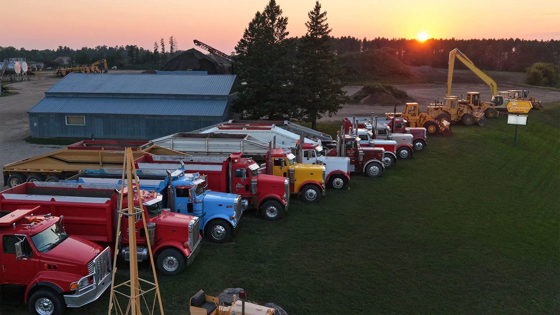Aerial view of the Storlie Construction dump truck and equipment fleet lined up in the yard at sunset near Cass Lake, Minnesota.